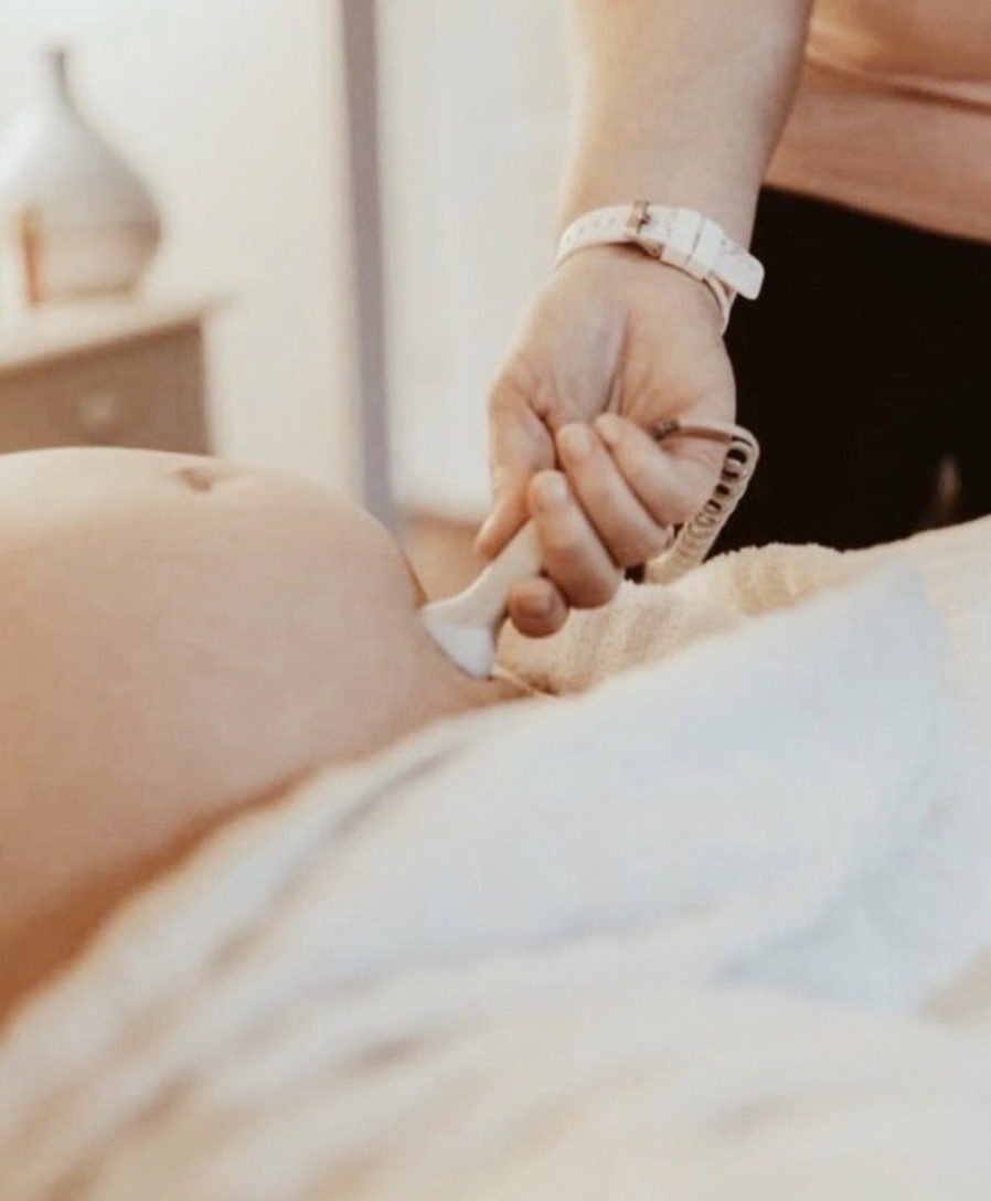A midwife listening to a baby's heartbeat with a Doppler during a prenatal visit